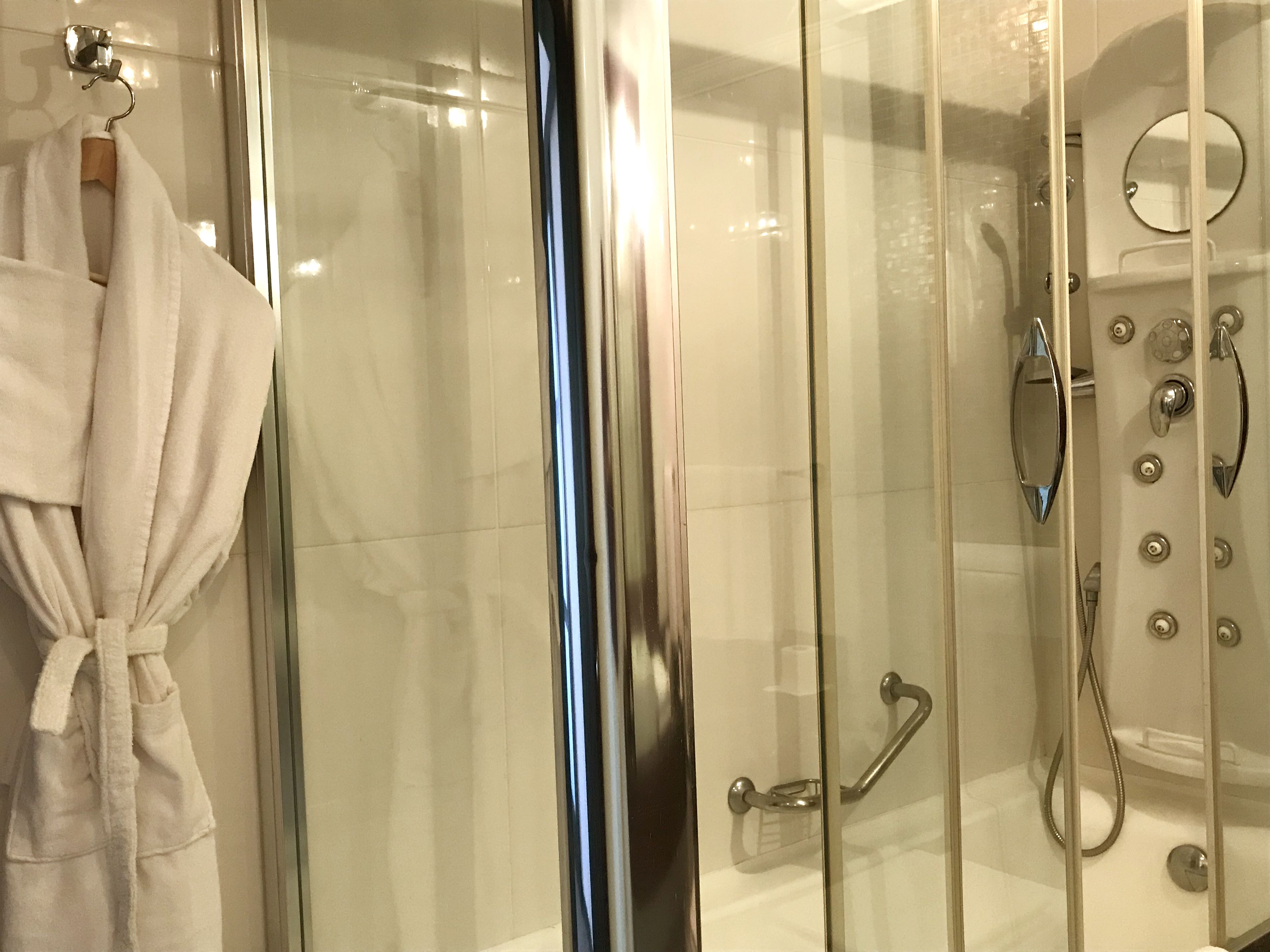 A modern bathroom with a glass shower enclosure, a white bathtub, and a towel rack with a white bathrobe.