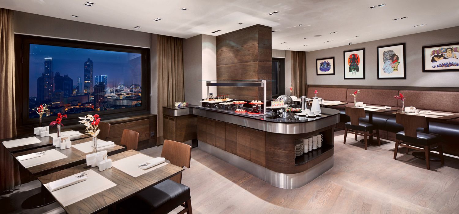 A modern hotel dining area with a central bar, seating arrangements, and a city view.