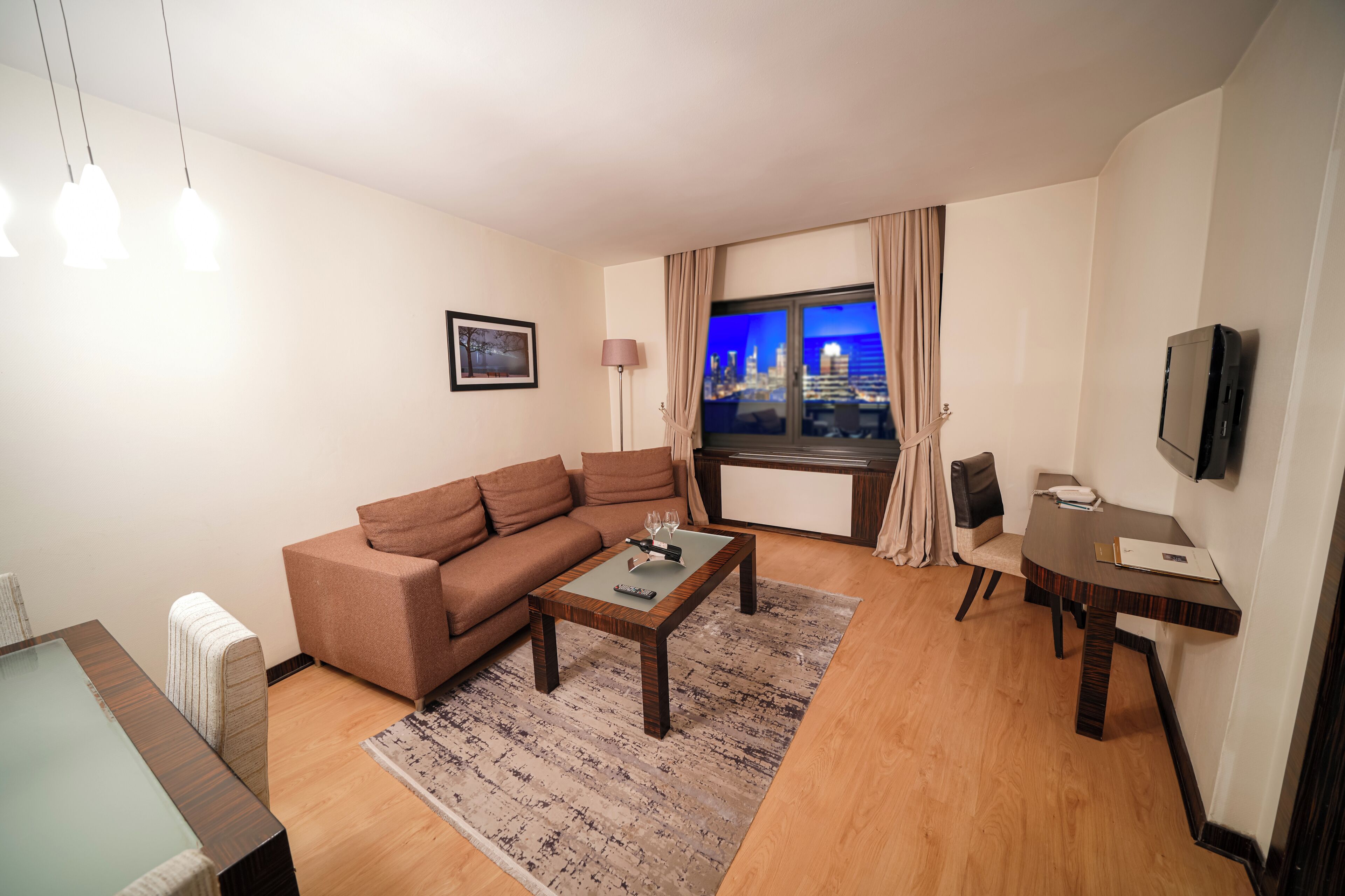A modern living room with a sofa, coffee table, TV, and a city view through the window.