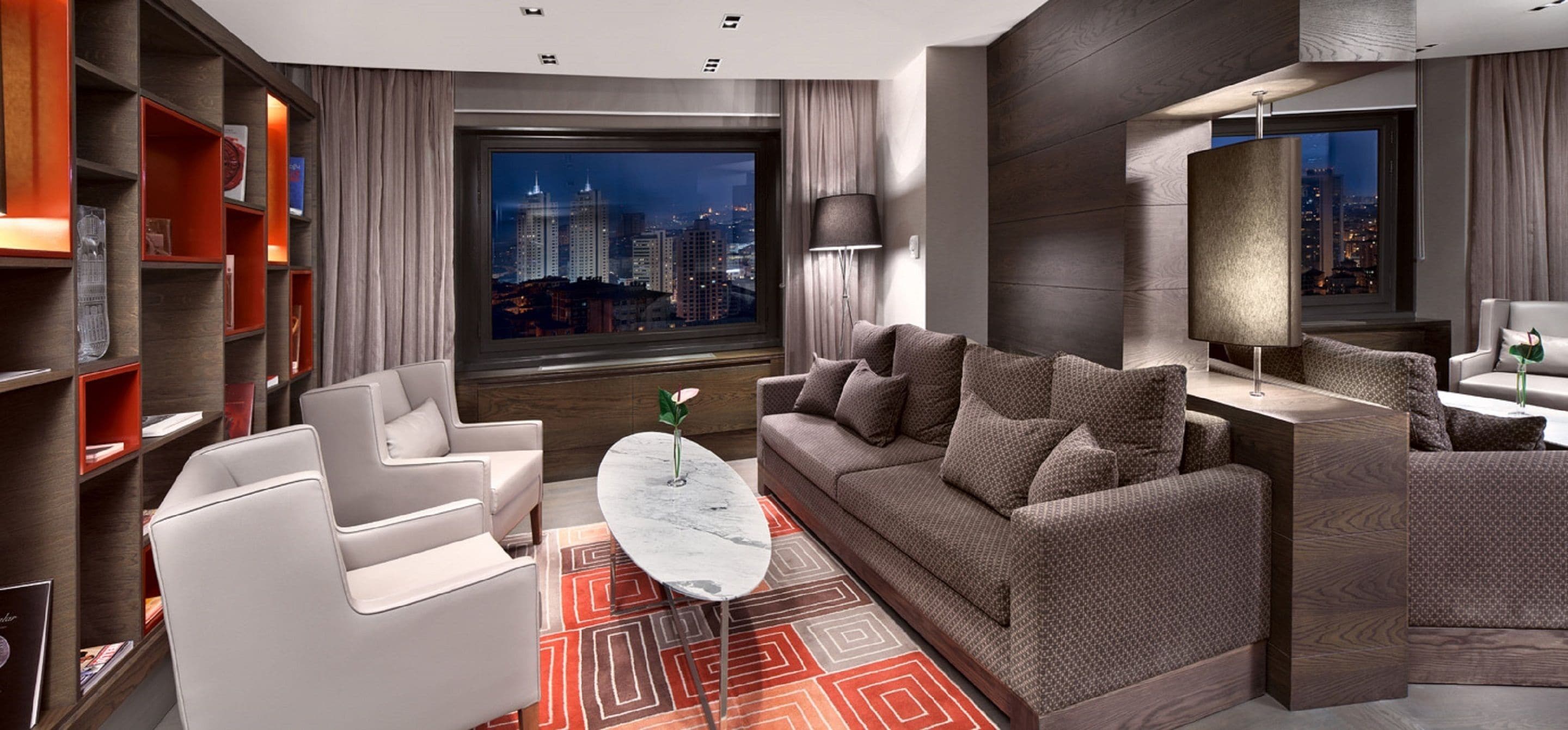 A modern living room with a sofa, armchairs, a coffee table, and a bookshelf.