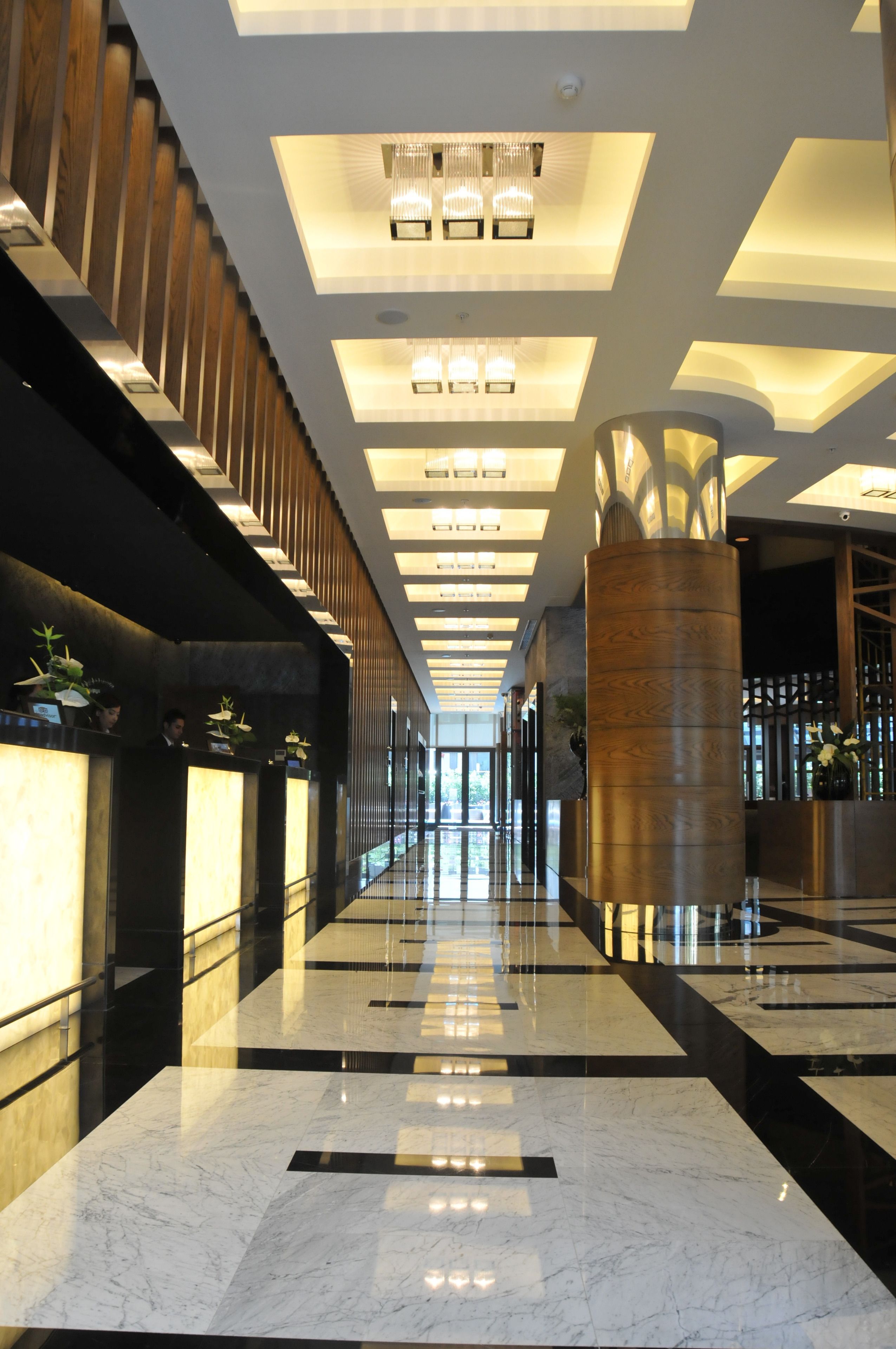 A modern hotel lobby with a long reception desk, a central column, and a high ceiling with recessed lighting.