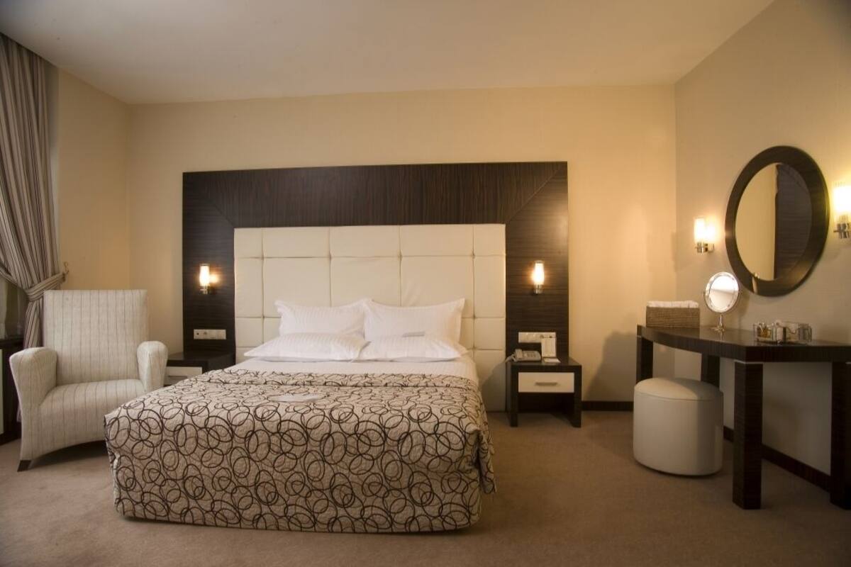A hotel room with a large bed, a bedside table, a chair, a desk, and a mirror.