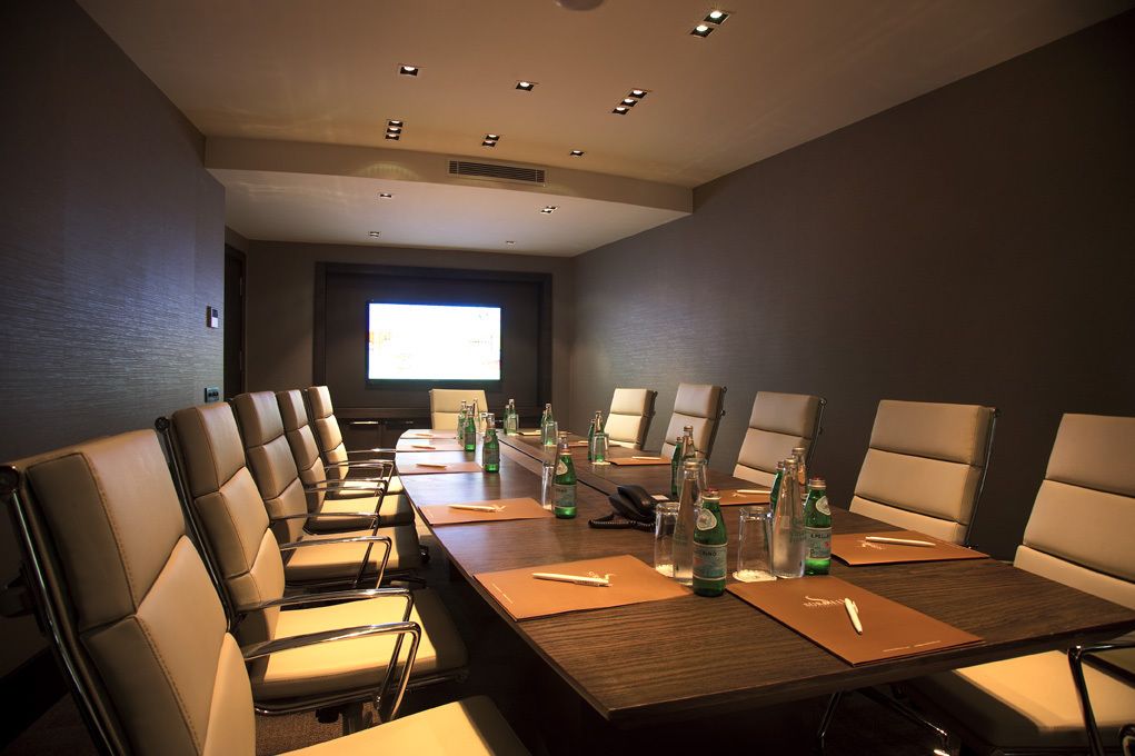 A conference room with a long table, multiple chairs, and a projector screen.