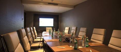 A conference room with a long table, multiple chairs, and a projector screen.