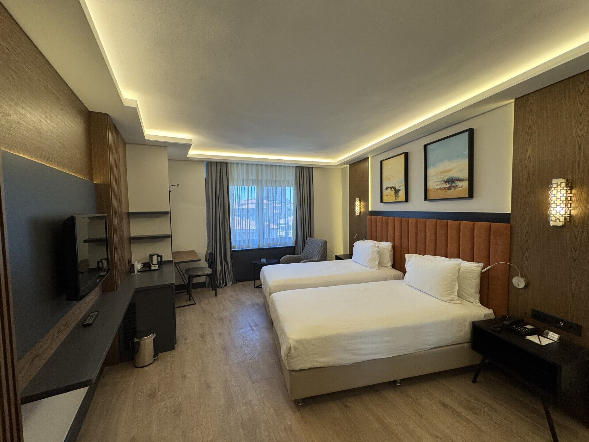 A hotel room with two beds, a desk, a TV, and a window with curtains.