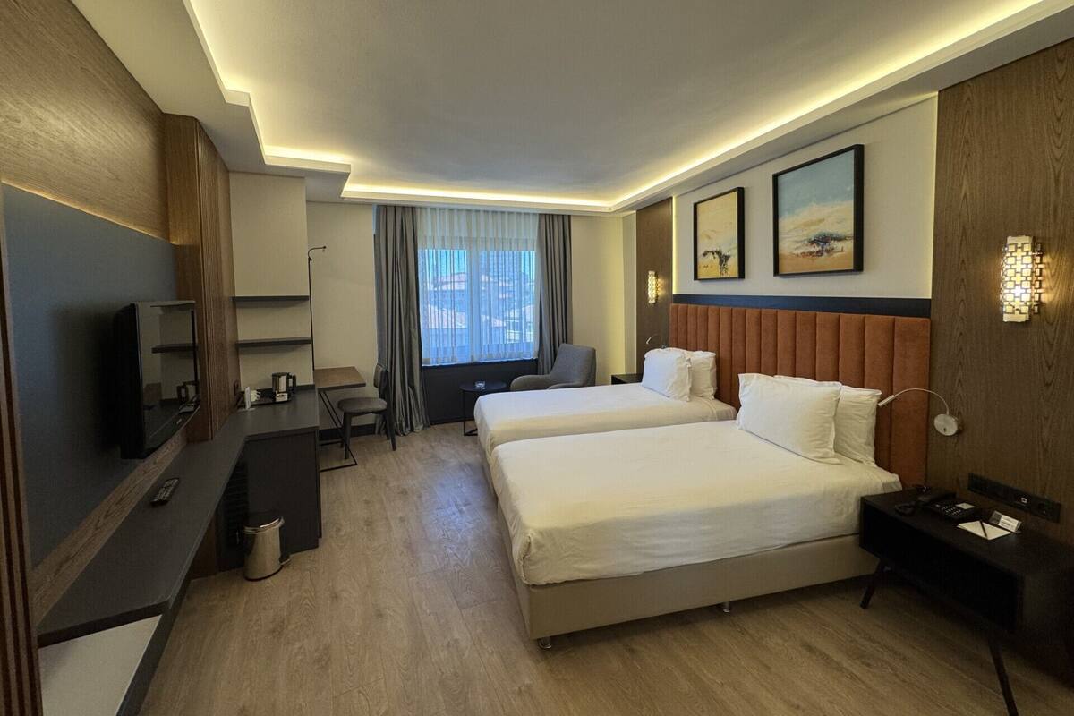 A hotel room with two beds, a desk, a TV, and a window with curtains.