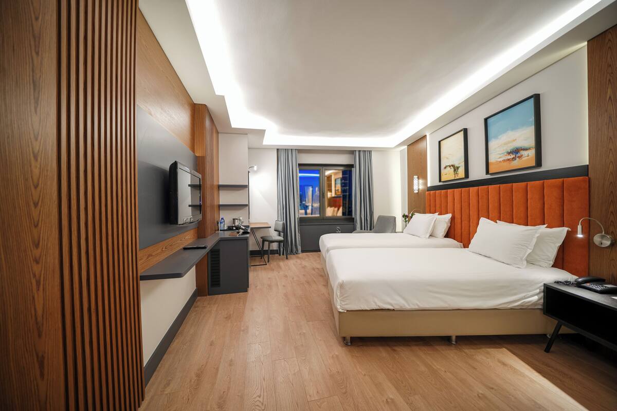 A hotel room with a bed, a desk, a TV, and a view of the city.