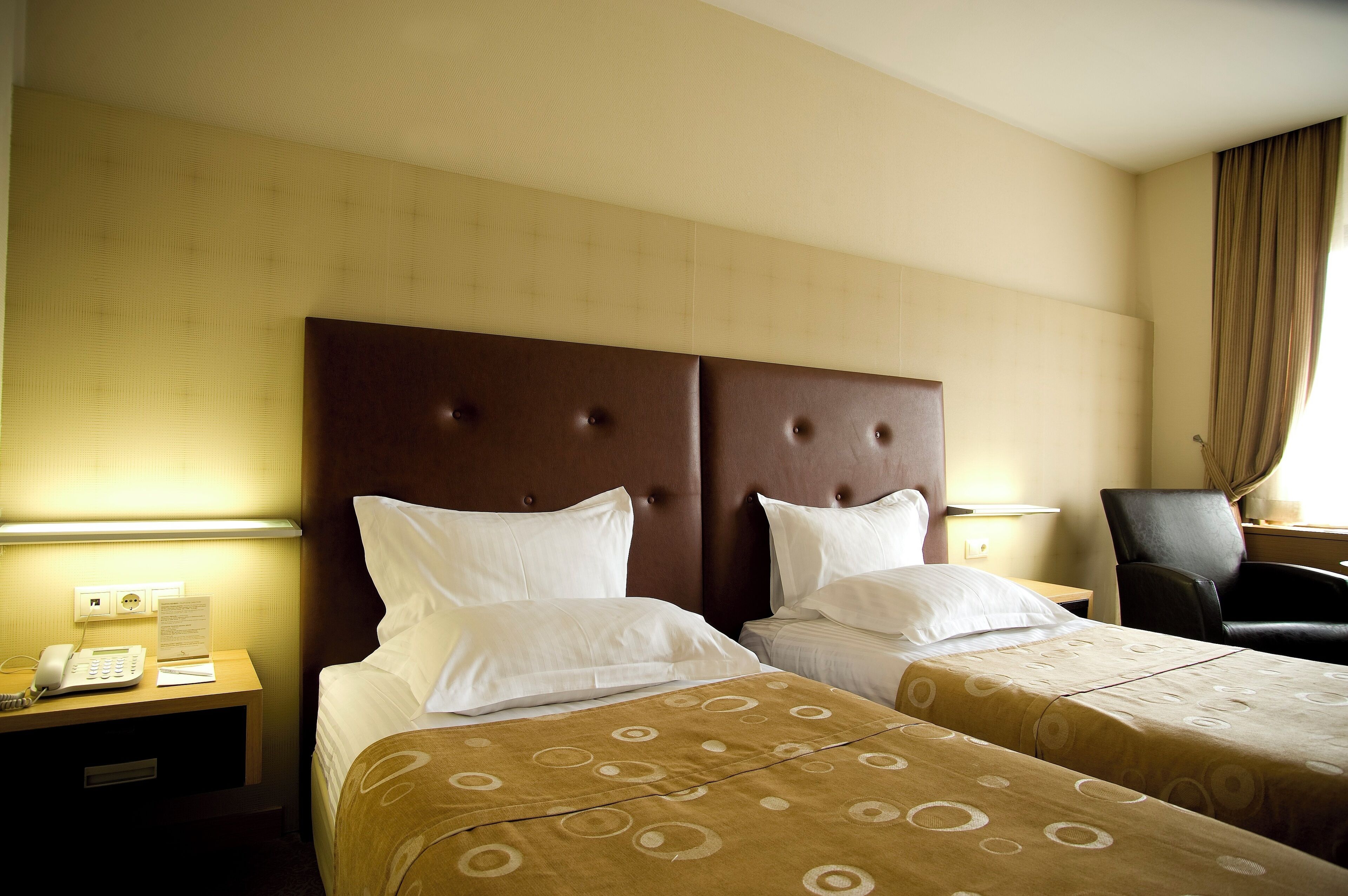 A hotel room with two beds, a headboard, a desk with a phone, and a chair.