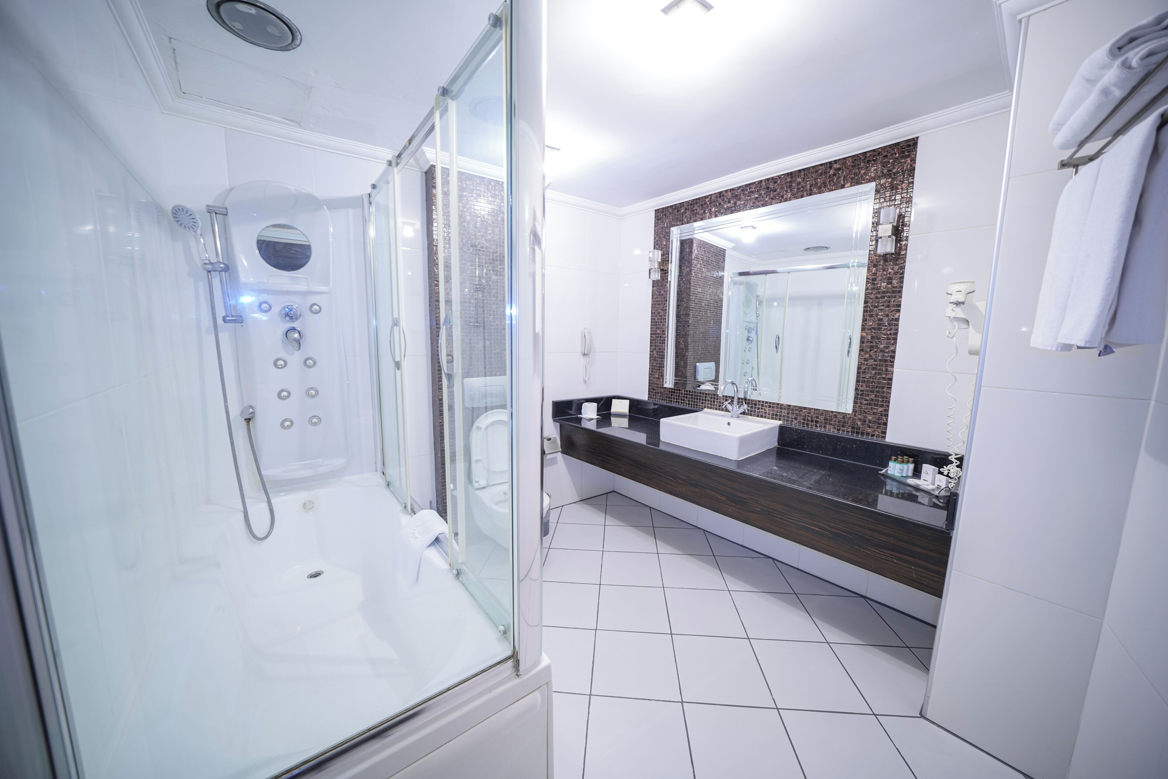 Ein modernes Badezimmer mit einer gläsernen Duschkabine, einem Waschbecken und einem großen Spiegel mit Mosaikrückwand.