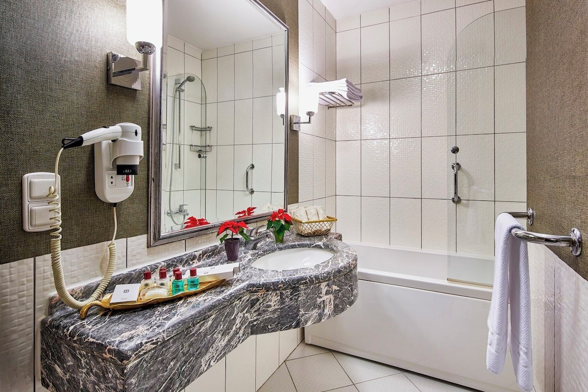 A bathroom with a marble sink, a hairdryer, a mirror, a bathtub, and a towel rack.