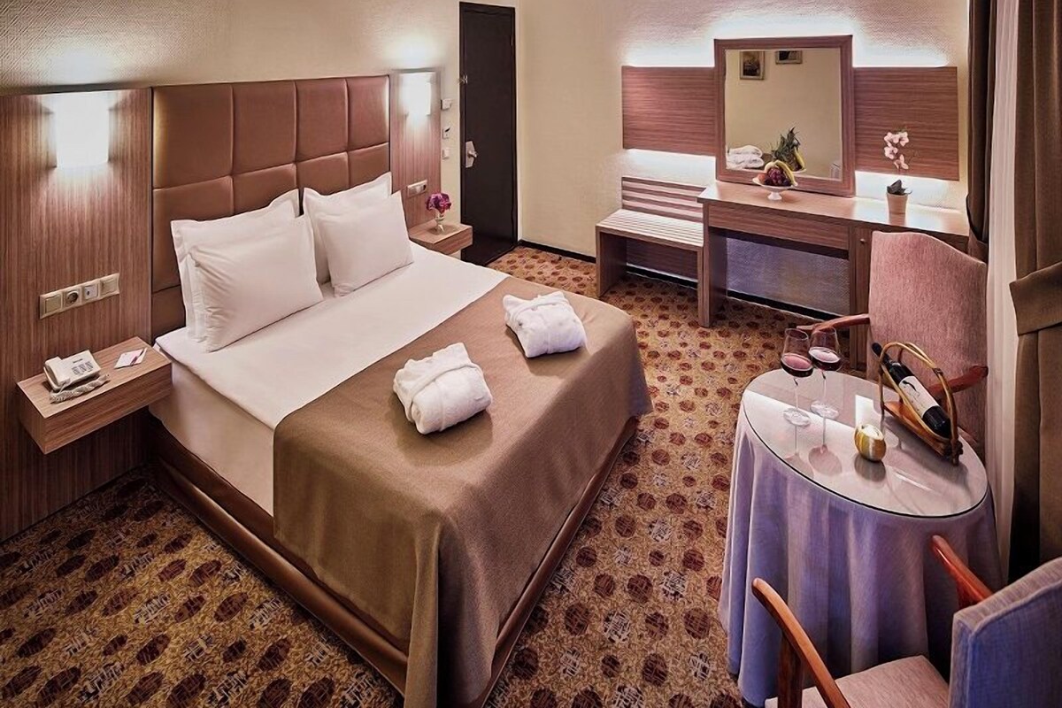 A hotel room with a bed, bedside table, a desk with a chair, a round table with a chair, and a mirror.