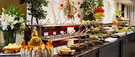 A buffet with various food items and decorative plants.