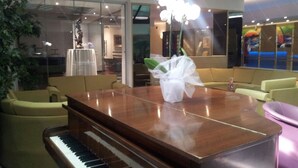 A modern interior with a wooden piano, beige sofas, and a white vase with a plant. - Gunes Hotel Merter (Istanbul)