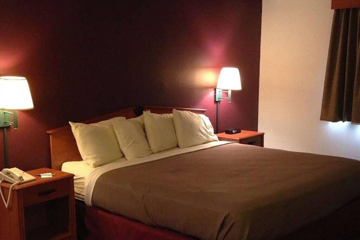 A hotel room with a bed, two bedside lamps, a nightstand with a phone, and a window with curtains.