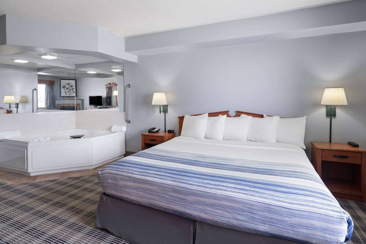 A hotel room with a large bed, a separate bathroom with a bathtub, and two bedside tables with lamps.