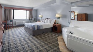 Una habitación de hotel con cama, mesita de noche, lámpara y un ventanal grande.