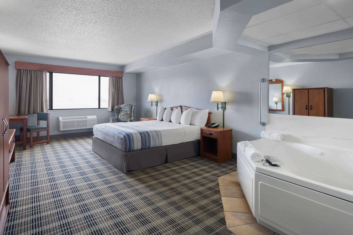 A hotel room with a bed, bedside table, lamp, and a large window.