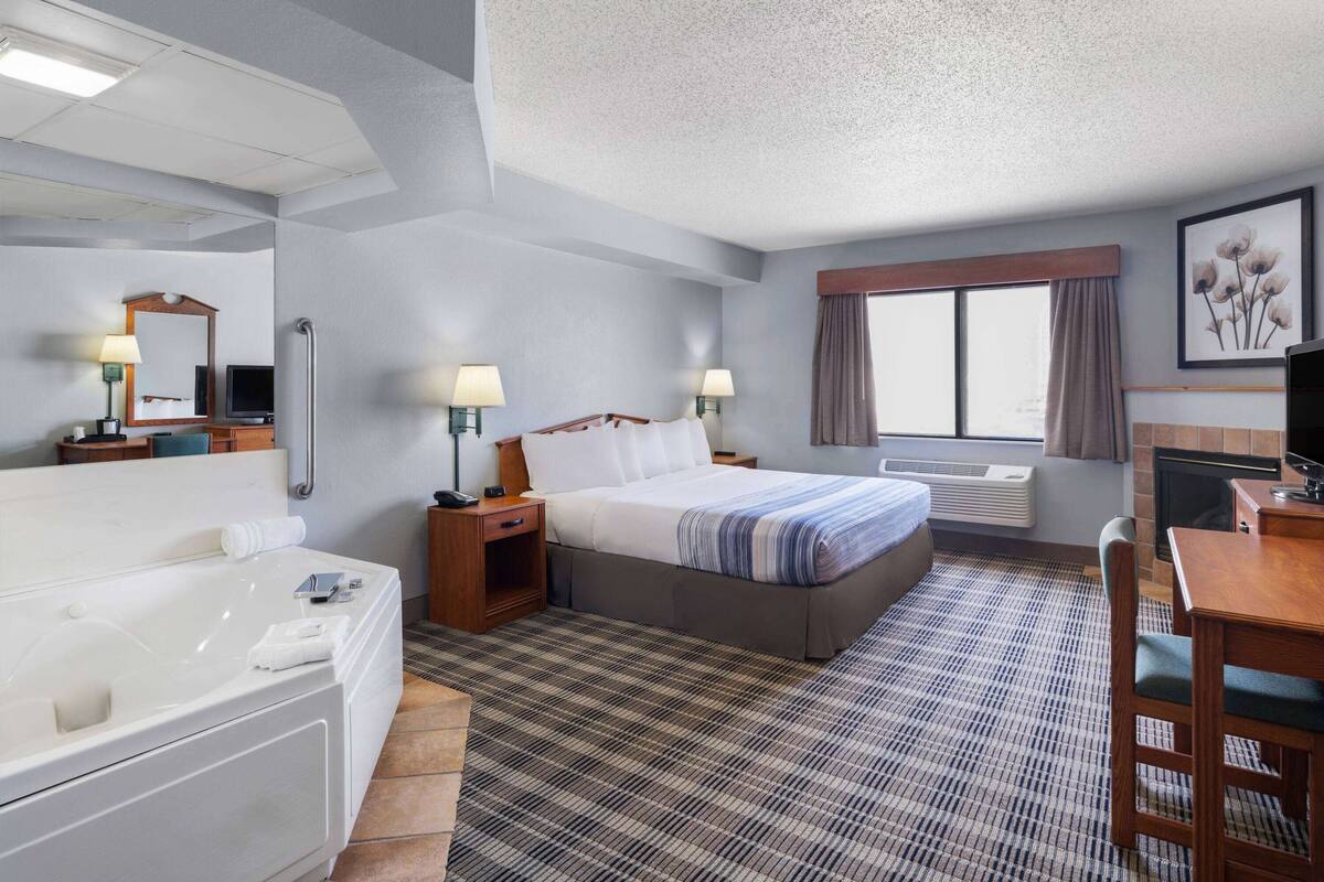 A hotel room with a large bed, a separate bathroom with a bathtub, a desk with a chair, and a television.