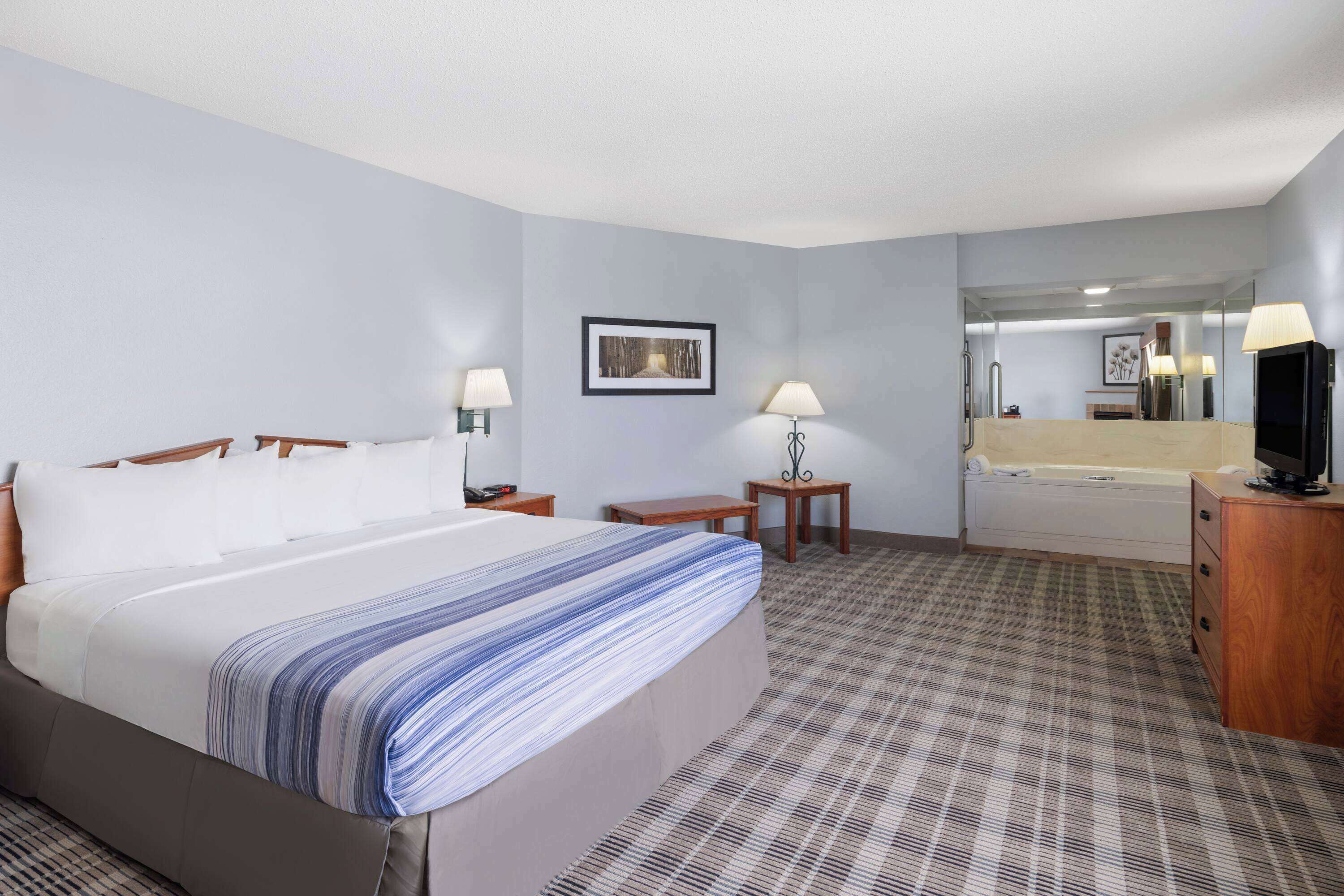 Une chambre d’hôtel équipée d’un lit, d’un bureau, d’une chaise, d’une petite table, d’un miroir et d’un téléviseur.