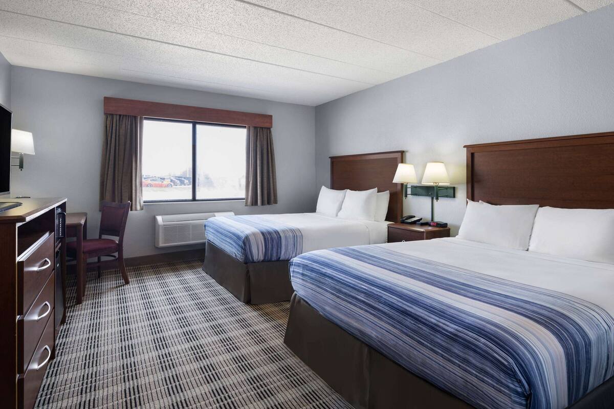 A hotel room with two beds, a desk, a chair, and a window with curtains.
