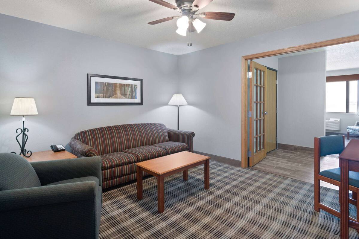 A hotel room with a striped sofa, a wooden coffee table, a lamp, a ceiling fan, and a door leading to another room.