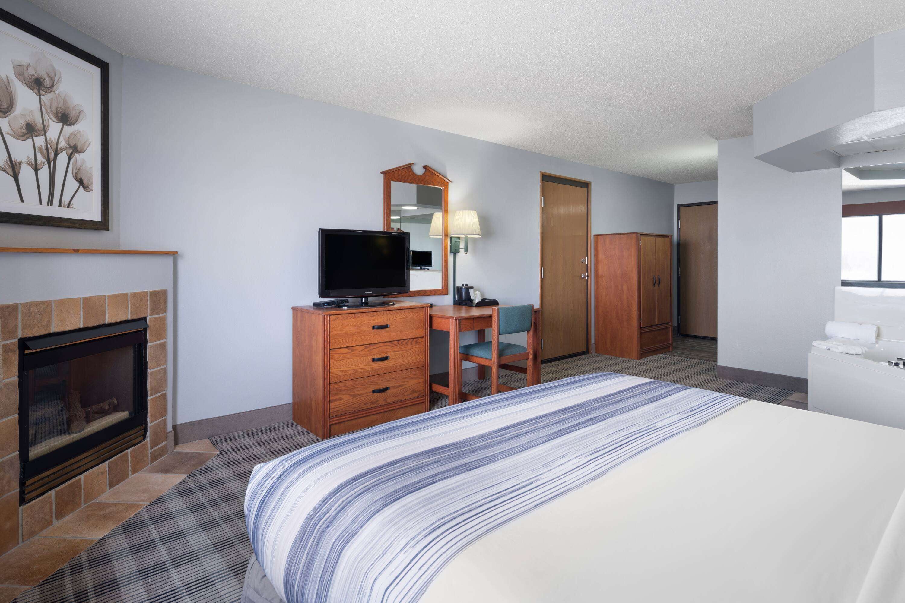 A hotel room with a bed, a television, a desk with a chair, a mirror, a wardrobe, and a fireplace.