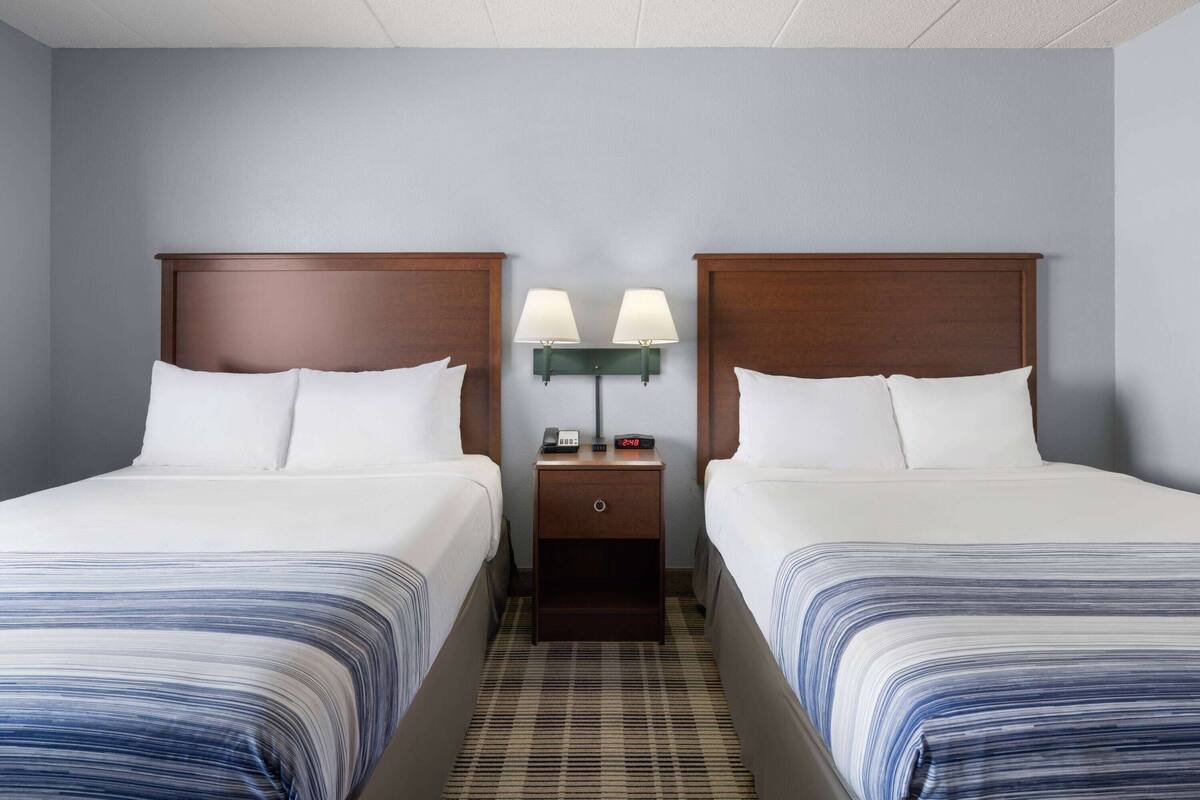 A hotel room with two beds, a nightstand with lamps, and a plaid-patterned carpet.