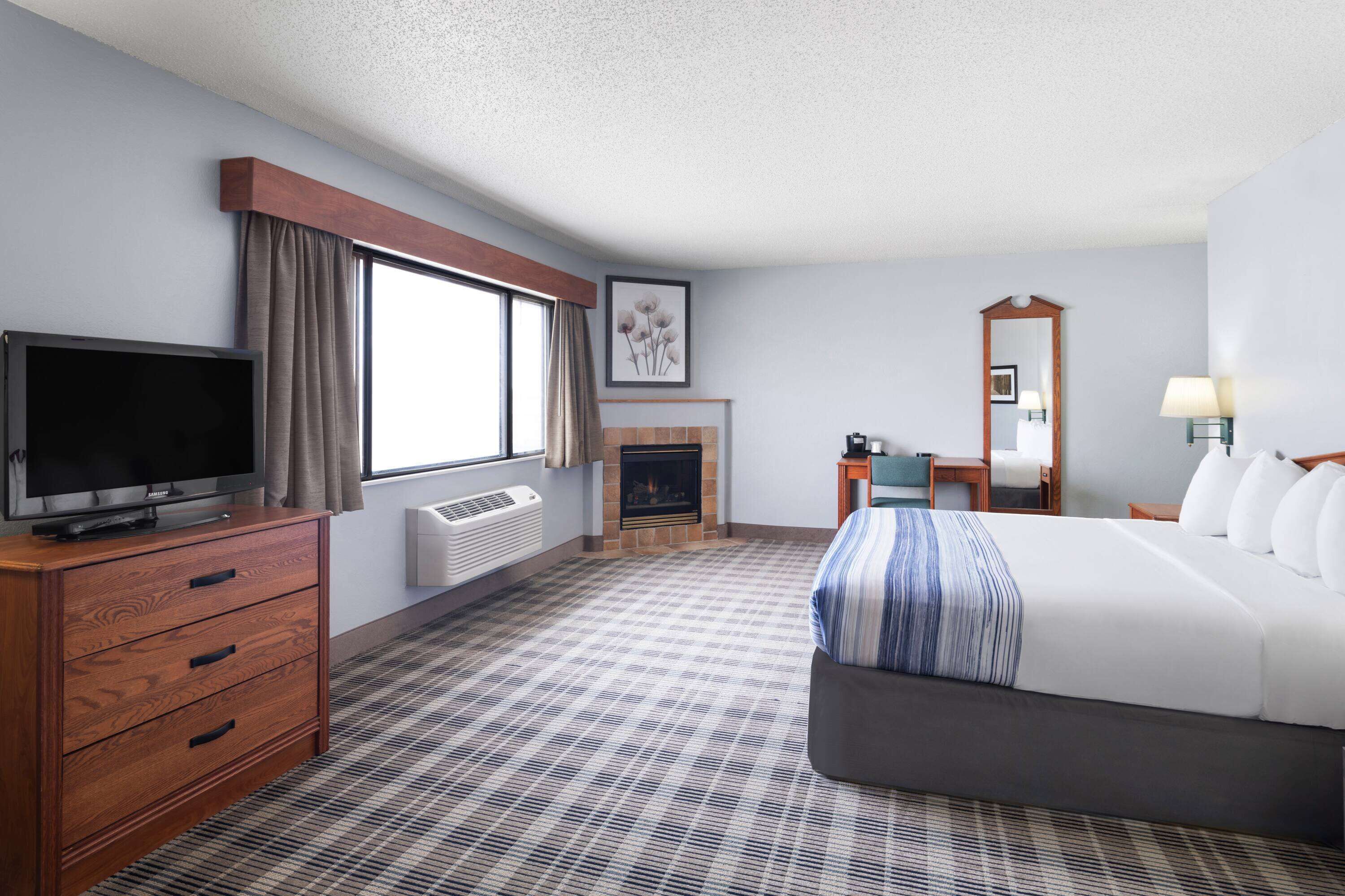 Une chambre d’hôtel avec un lit, une télévision, une cheminée, un bureau et une fenêtre.
