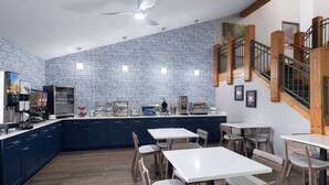 Una cocina moderna con armarios azul oscuro, encimeras blancas y un salpicadero de azulejos. Hay varias mesas y sillas dispuestas para comer.