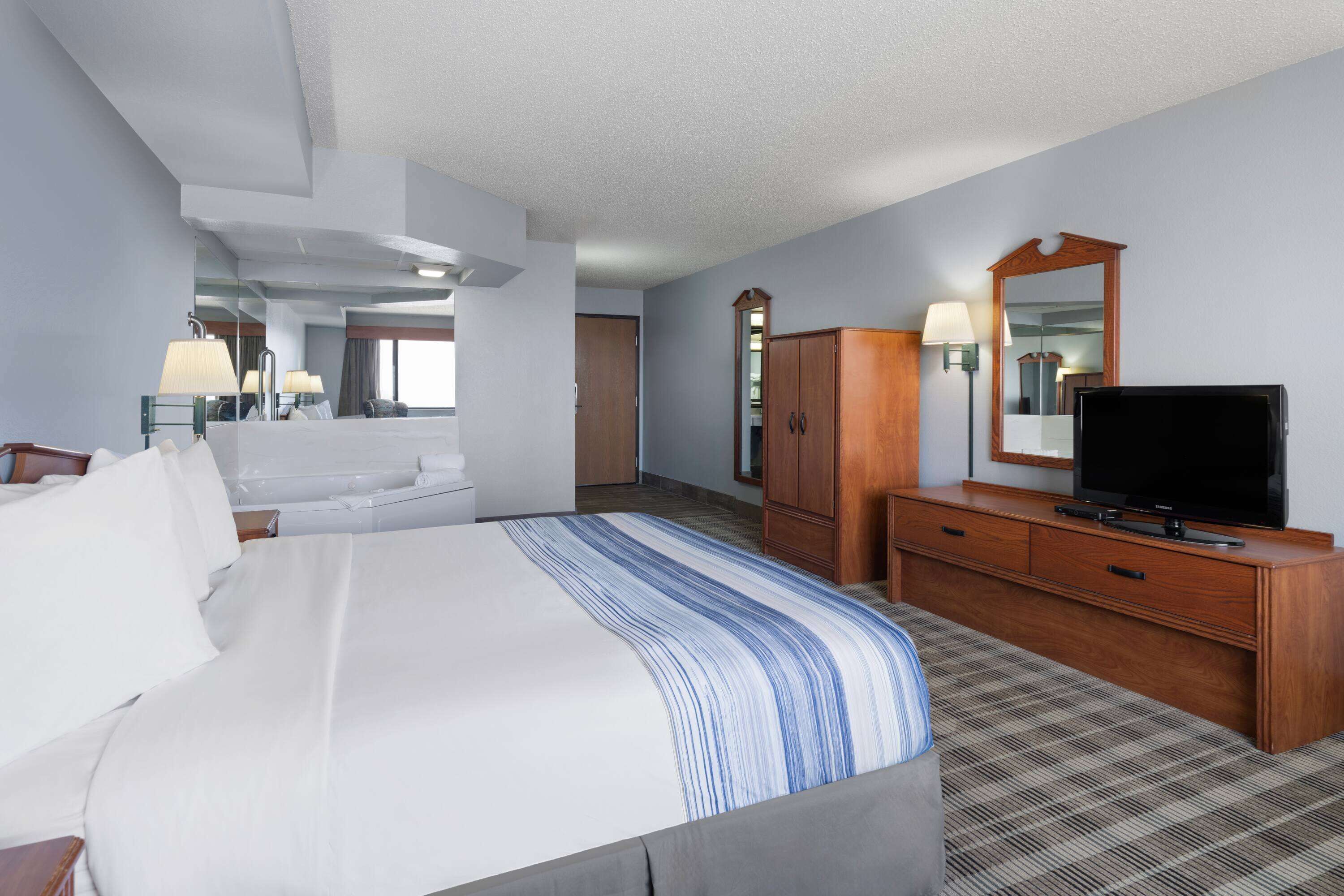 Une chambre d’hôtel avec un grand lit, une commode en bois, une télévision et un miroir.
