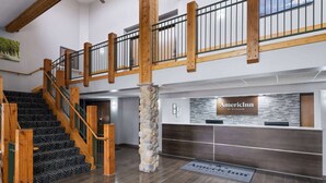 Zona de recepción con un pilar de piedra, mostrador de recepción y una escalera con barandillas de madera.