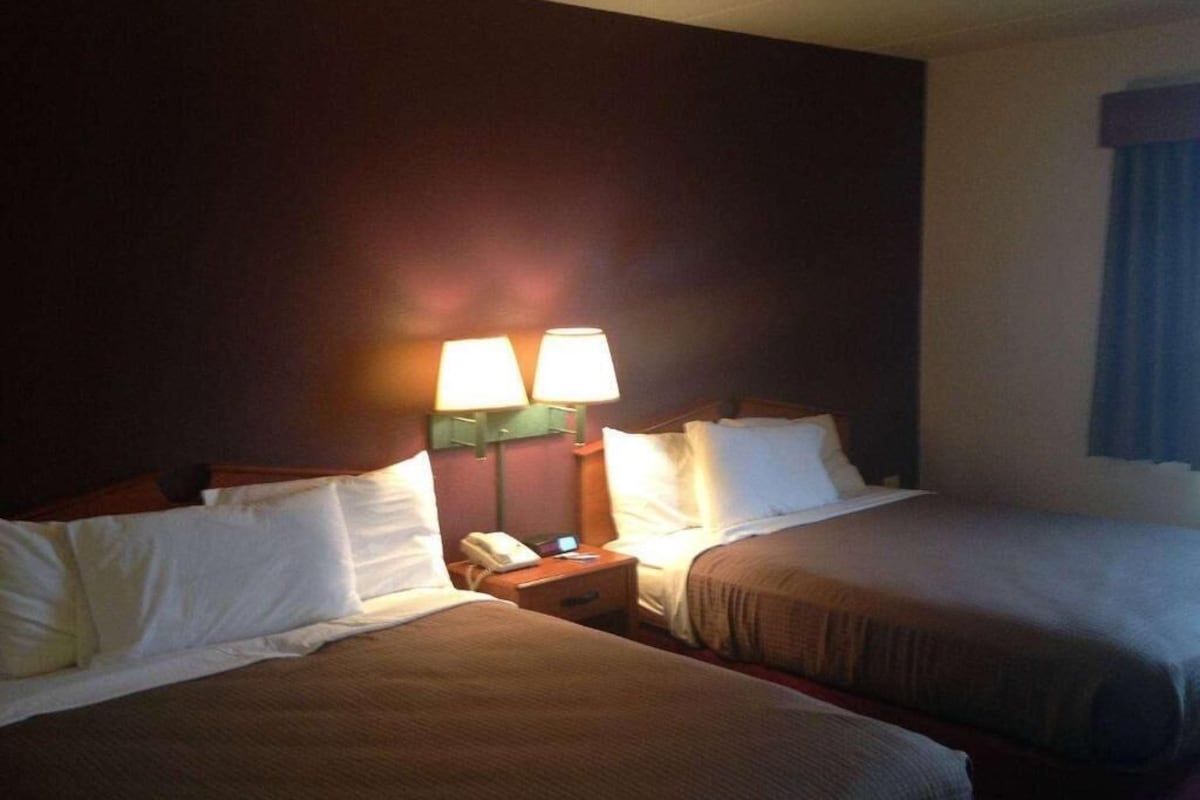 A hotel room with two beds, a nightstand with a phone, and a lamp.