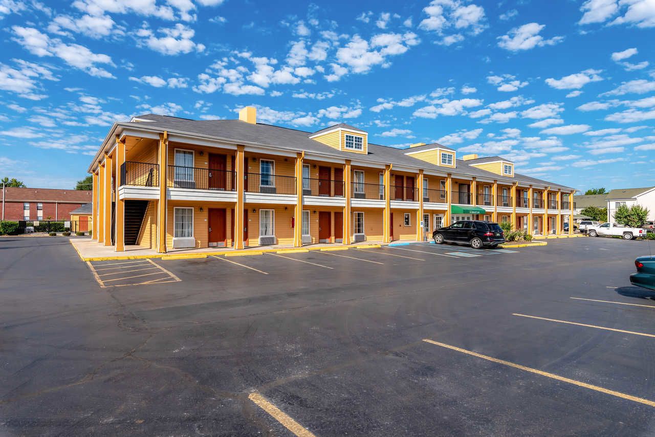 A motel with multiple rooms, a parking lot, and a clear blue sky.