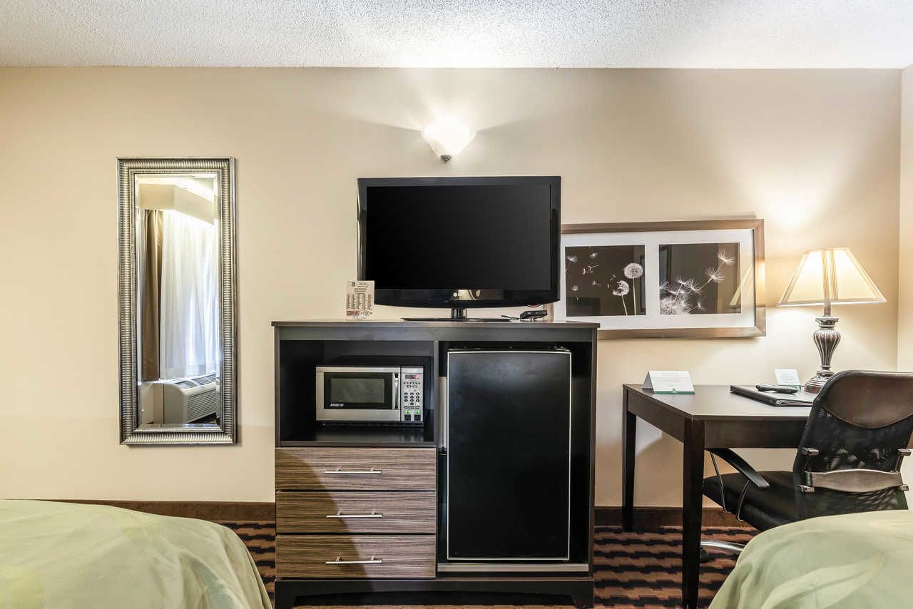 Habitación de hotel con cama, televisión, microondas, refrigerador, escritorio y una silla.