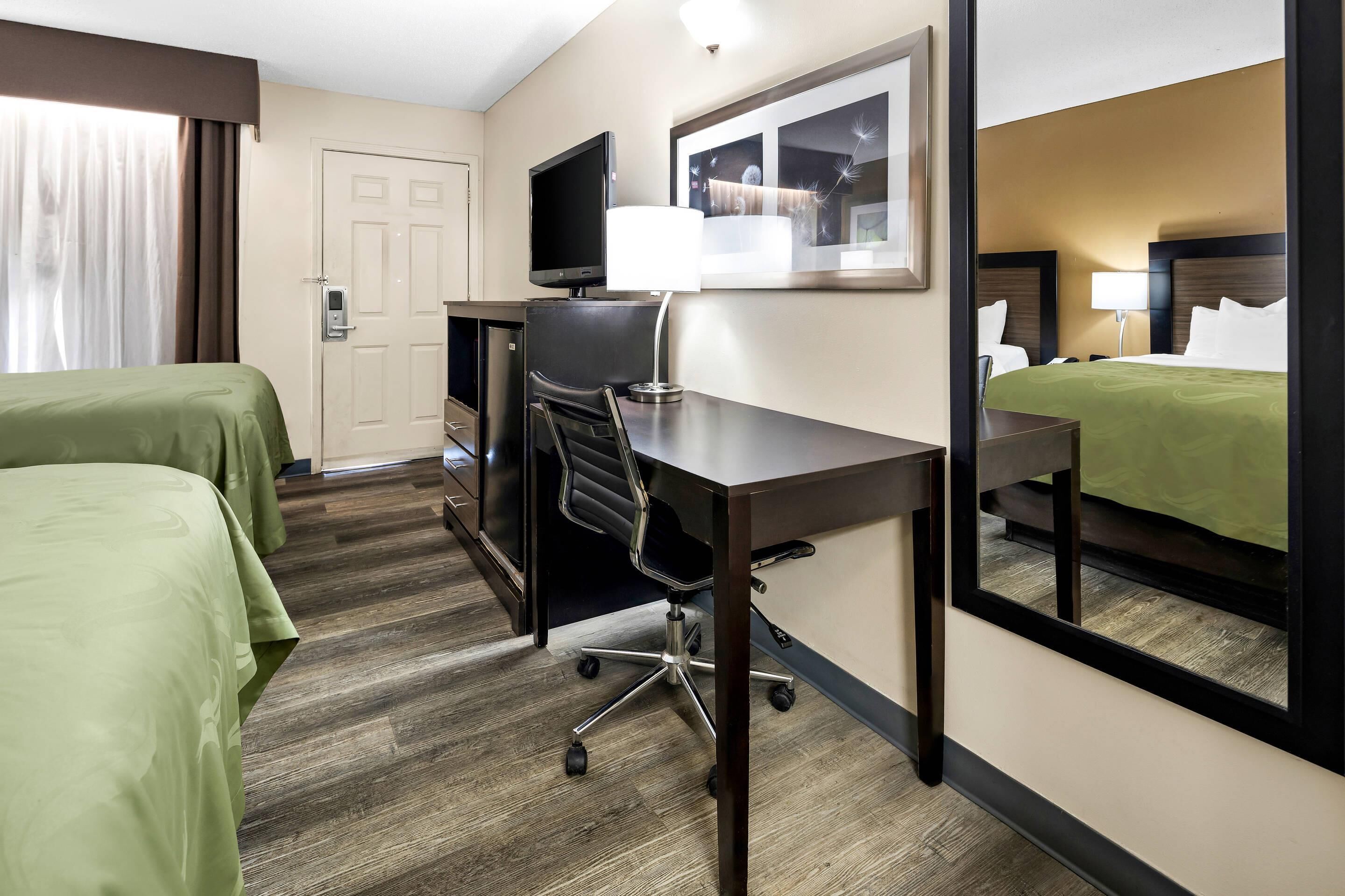 A hotel room with two beds, a desk, a chair, a TV, and a window with a view.