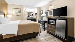 A hotel room with a bed, desk, TV, microwave, and refrigerator.
