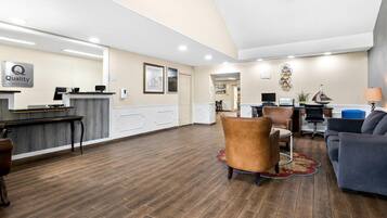 Un espace d’accueil d’hôtel comprenant un comptoir de réception, un ordinateur, une imprimante et un coin salon avec un canapé et des fauteuils.