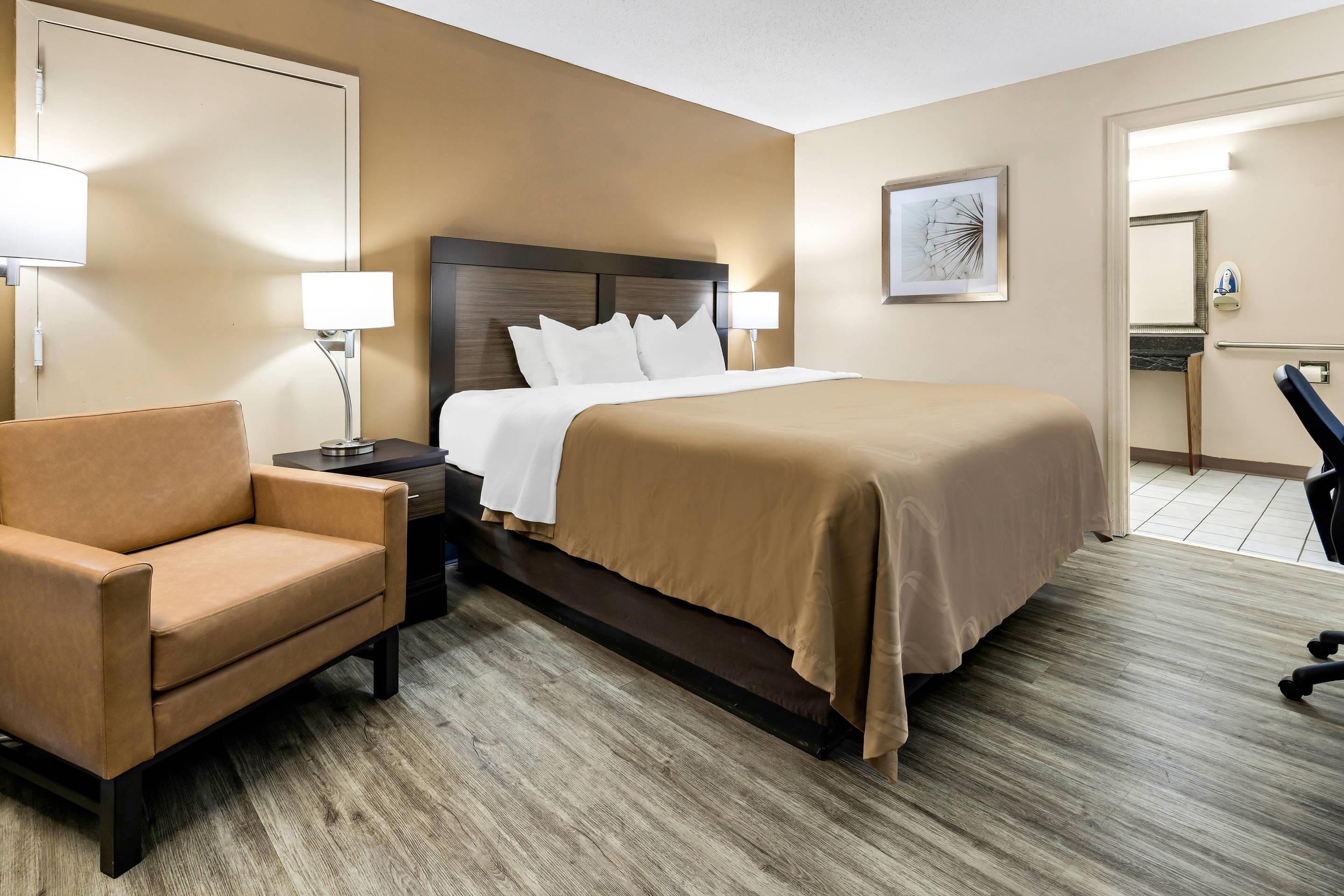 A hotel room with a bed, a chair, a nightstand, and a desk.