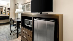 A compact kitchenette with a microwave, refrigerator, and a flat-screen TV mounted on the wall.