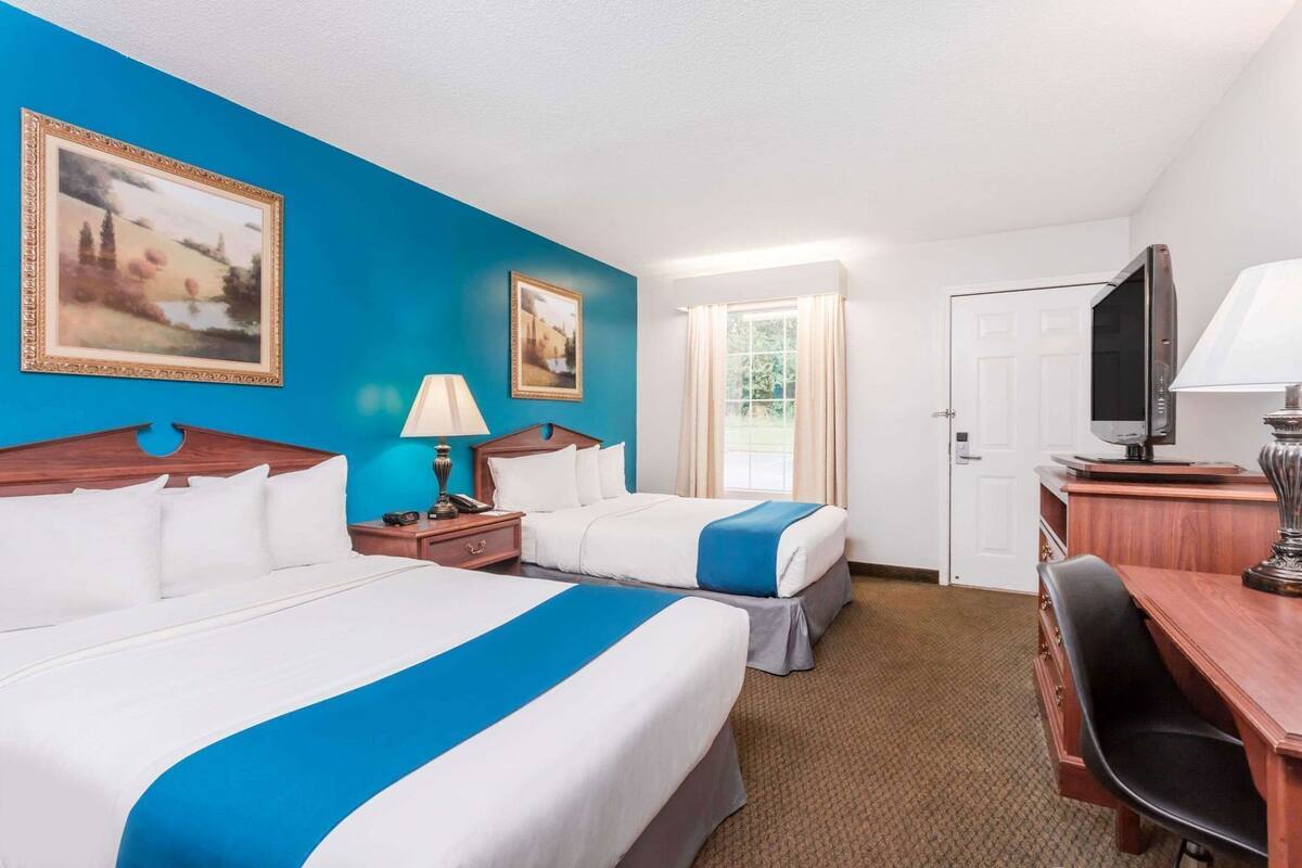 Een hotelkamer met twee bedden, een bureau, een televisie en twee schilderijen aan de muur.