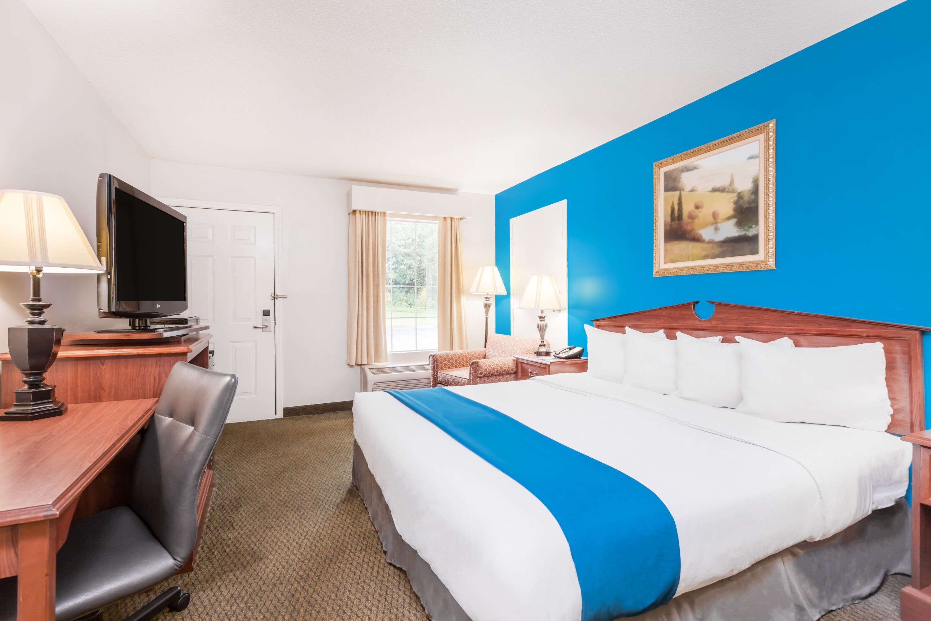 Ein Hotelzimmer mit Bett, Schreibtisch, Fernseher und einem Bild an der Wand.