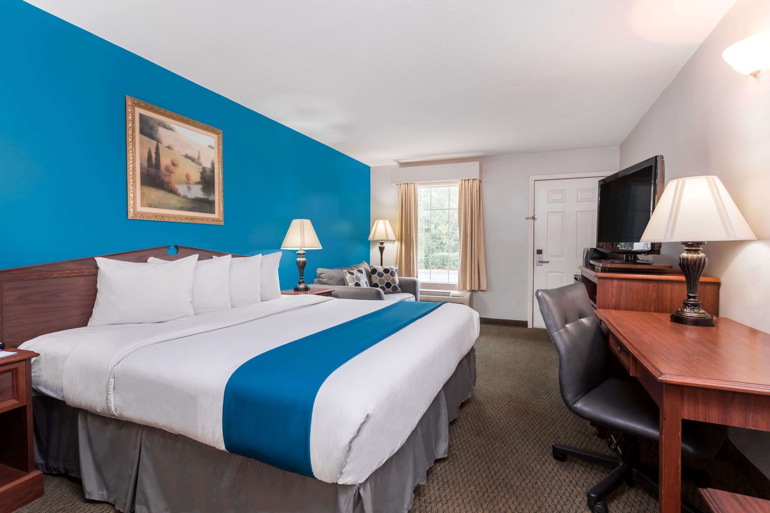 A hotel room with a large bed, two bedside tables, a desk, a chair, a television, and a window with curtains.