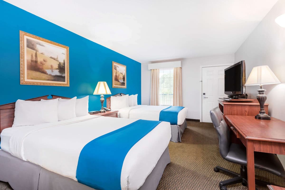 Een hotelkamer met twee bedden, een bureau, een stoel, een televisie en twee schilderijen aan de muur.