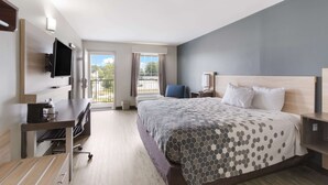 A hotel room with a large bed, a desk, a TV, and a balcony with a view of the outdoors. - Econo Lodge Greenville near University (Greenville)
