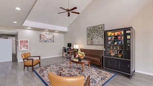 A spacious living area with a brown leather sofa, a coffee table, and a patterned rug. A vending machine is visible on the right side. - Econo Lodge Greenville near University (Greenville)