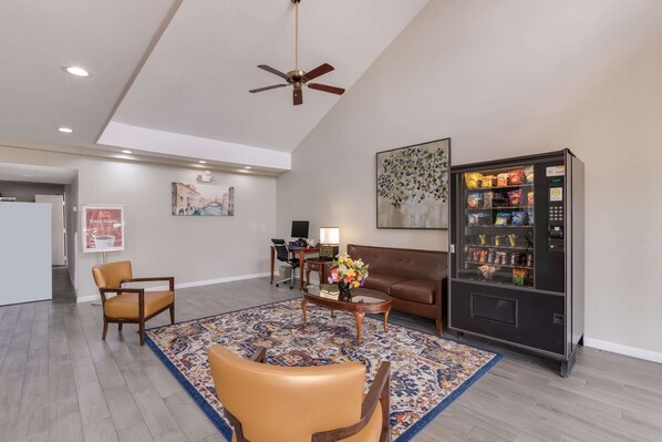 A spacious living area with a brown leather sofa, a coffee table, and a patterned rug. A vending machine is visible on the right side.