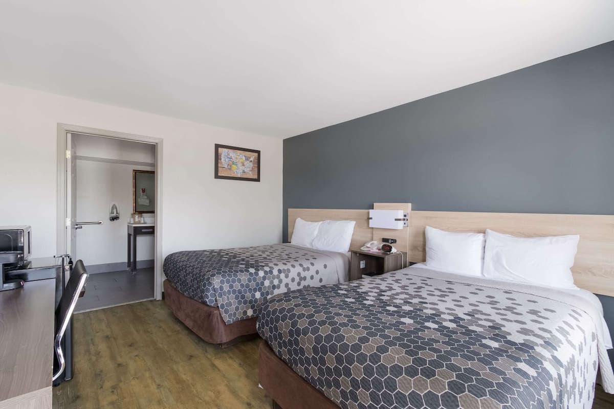 Ein Hotelzimmer mit zwei Betten, einem Schreibtisch, einem Stuhl, einem kleinen Tisch und einem Spiegel.