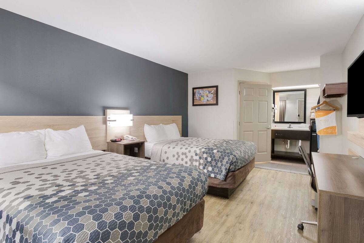 Ein Hotelzimmer mit zwei Betten, einem Schreibtisch, einem Stuhl, einem Fernseher und einer Badezimmertür.