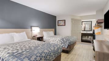 A hotel room with two beds, a desk, a chair, a TV, and a bathroom door.