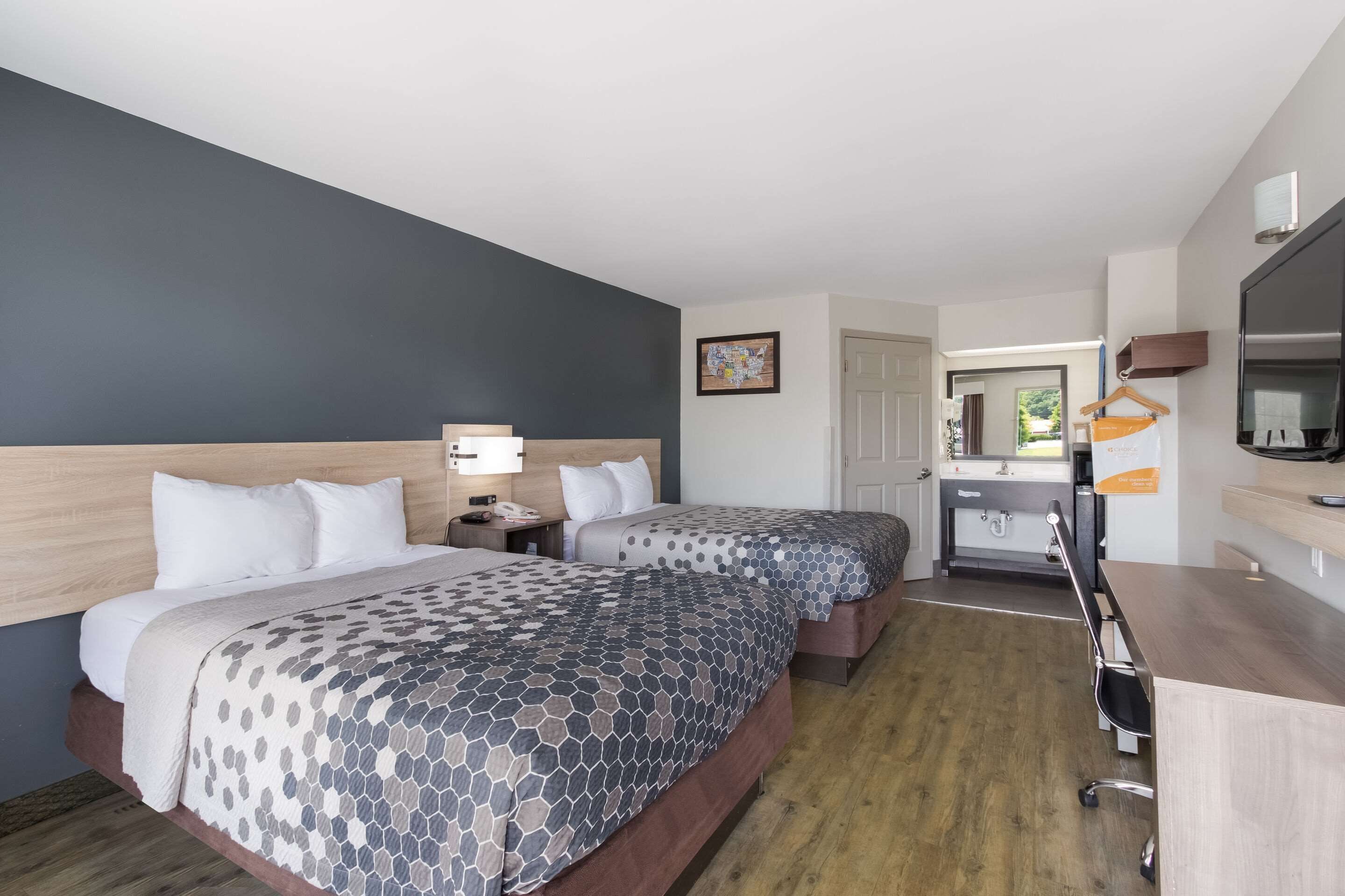 A hotel room with two beds, a desk, a chair, a TV, and a bathroom.